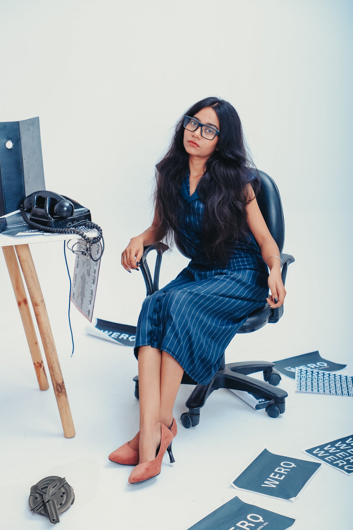 Woman sitting in a chair with office items around her, blue formal dress women, striped formal dress, sheath dress for office, formal office dress India, button down work dress, professional dress for women, calf-length formal dress, luxury office dress India, structured sheath dress, formal work dress women, formalwear for Indian women, blue striped dress office, power dressing dress, women’s workwear India, business formal dress, elegant formal dress, boardroom ready dress, modern work dress India,