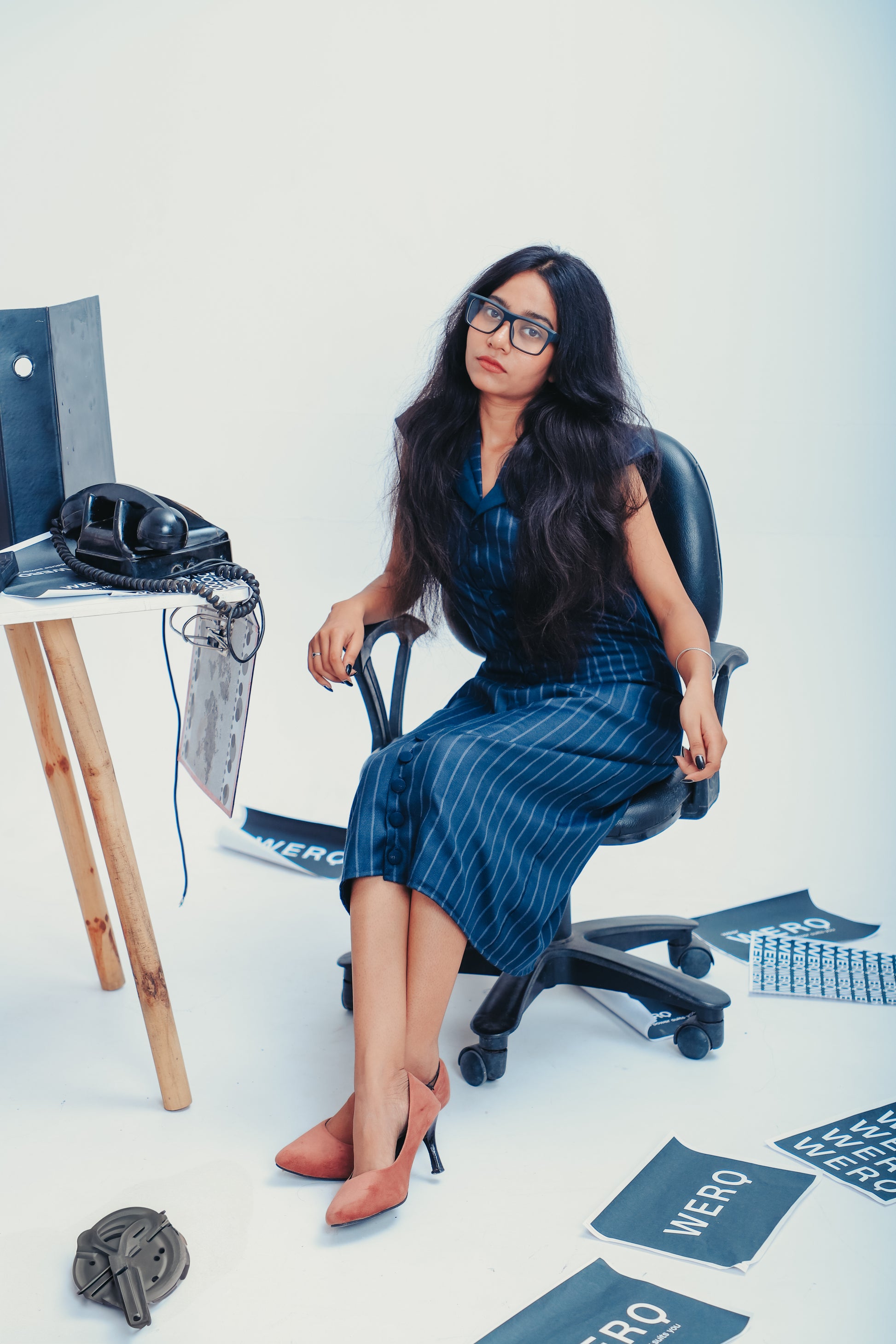 Woman sitting in a chair with office items around her, blue formal dress women, striped formal dress, sheath dress for office, formal office dress India, button down work dress, professional dress for women, calf-length formal dress, luxury office dress India, structured sheath dress, formal work dress women, formalwear for Indian women, blue striped dress office, power dressing dress, women’s workwear India, business formal dress, elegant formal dress, boardroom ready dress, modern work dress India,