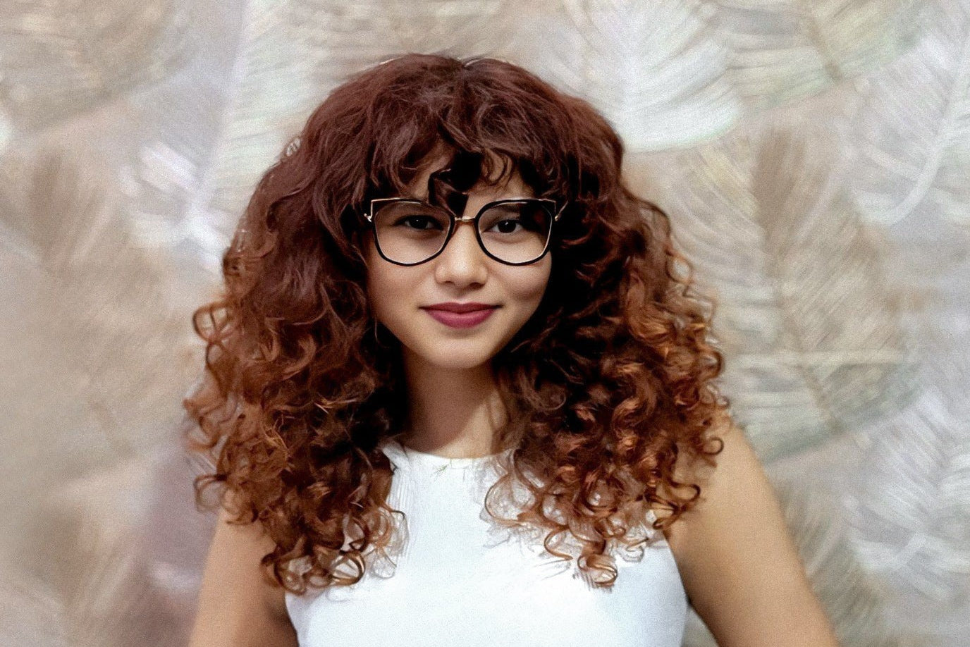 WERQ founder and creative director Priyanshi Singh. Woman with curly hair wearing glasses and a white top against a textured wall.